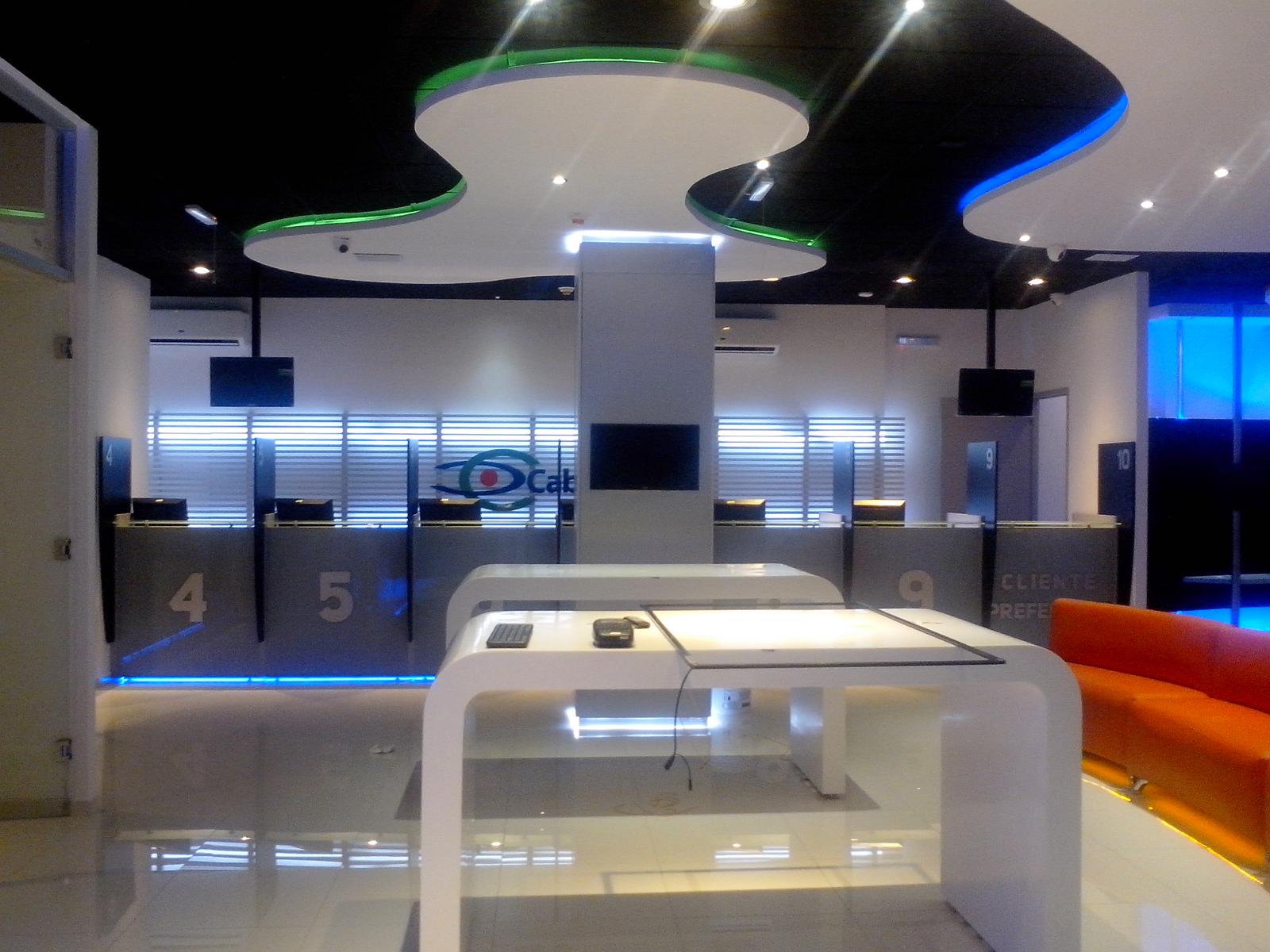 Interior de una sucursal Cablemás terminada: plafón curvo con luz verde y azul, mostradores y módulo de atención